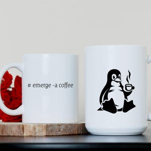 May include: Two white ceramic mugs with black text and a penguin graphic. The mug on the left says "# emerge - a coffee". The mug on the right has a penguin holding a cup of coffee.