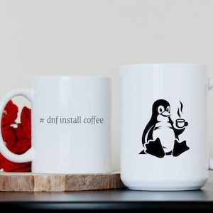 May include: Two white ceramic mugs. One mug has a black penguin holding a cup of coffee with steam rising from it. The other mug has the text "# dnf install coffee" printed on it.