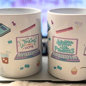 Könnte beinhalten: Zwei weiße Keramikbecher mit bunten Designs. Ein Becher zeigt einen Laptop mit dem Text "Working from Home" und der andere Becher zeigt einen Laptop mit dem Text "Work in Progress".