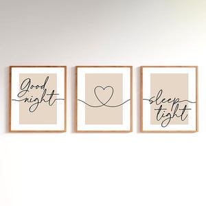 Op de afbeelding: Drie ingelijste wandkunstprints. De eerste print zegt "Good night" in cursief. De tweede print heeft een lijntekening van een hart. De derde print zegt "sleep tight" in cursief. Alle prints hebben een beige achtergrond.