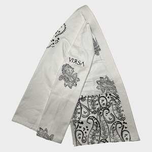 Puede incluir: Bufanda blanca con estampado de cachemira negro y la palabra "VIRSA" impresa en negro. La bufanda tiene una textura acanalada y está doblada en forma triangular. El diseño de cachemira se presenta en los extremos y en el centro.