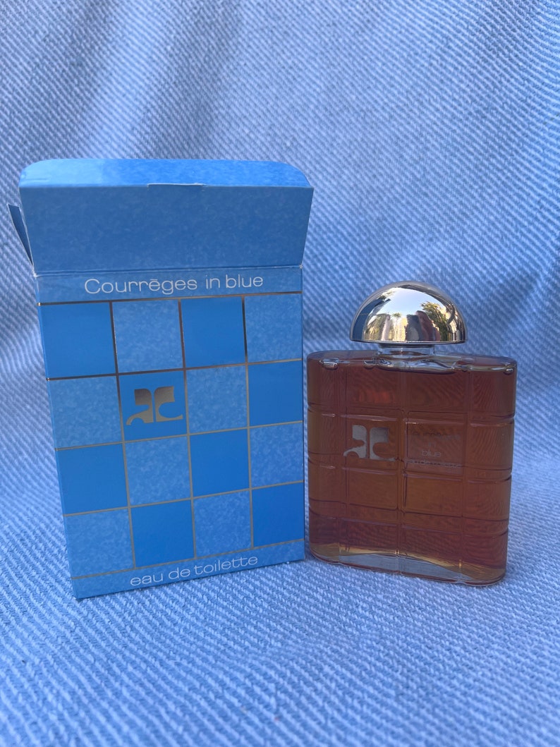 May include: A blue box with the text "Courreges in blue" and "eau de toilette" on it. The box contains a clear glass bottle of perfume with a silver cap. The bottle has a grid pattern and the letter "C" on the front.