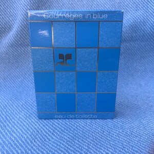 May include: A blue and silver box with the text "Courreges in blue" and "eau de toilette" on it. The box has a grid pattern and the letter "C" in a stylized font.