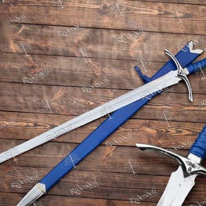 May include: Two silver swords with blue handles and scabbards. The swords are lying on a wooden surface.