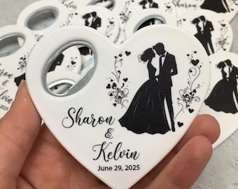 May include: White heart-shaped bottle opener with a silver opener and a black and white silhouette of a couple. The names "Sharon & Kelvin" and the date "June 29, 2025" are printed on the opener. Wedding favors.