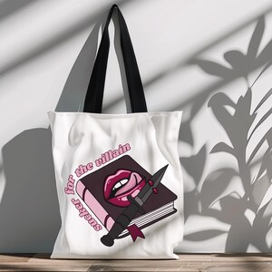 May include: White canvas tote bag with black handles. The bag features a pink and black graphic of a book with a knife and a red, open mouth with a tongue sticking out. The text "sucker for the villain" is written in pink on the bag.