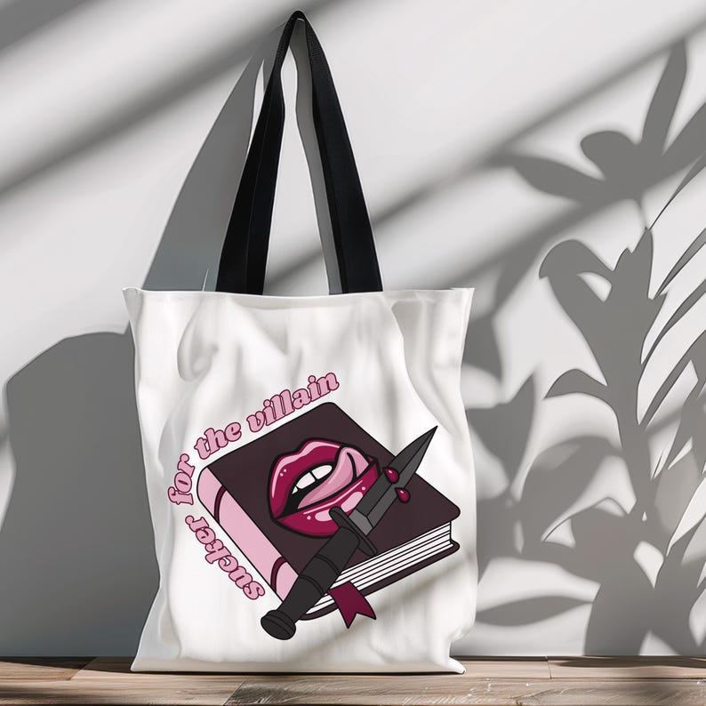 May include: White canvas tote bag with black handles. The bag features a pink and black graphic of a book with a knife and a red, open mouth with a tongue sticking out. The text "sucker for the villain" is written in pink on the bag.