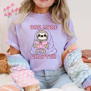 A purple t-shirt showing the one more chapter png design. A cozy sloth reading a book.