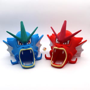 Op de afbeelding: Twee plastic figuren van de Pokémon Gyarados, een blauwe en een rode, met open monden en scherpe tanden. De blauwe Gyarados heeft een groene vin op zijn kop, terwijl de rode Gyarados een rode vin heeft.