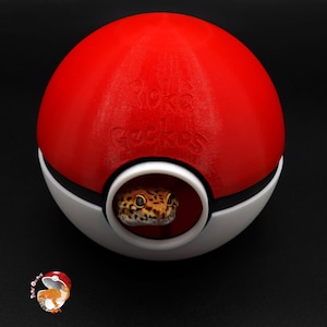 Può includere: Una Poké Ball rossa e bianca con il testo "Poke Gecko" in rilievo sulla parte superiore. Un geco spunta dall'apertura della Poké Ball.
