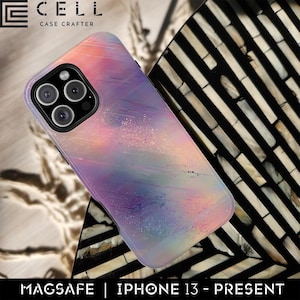 May include: A colorful phone case with a watercolor design in shades of pink, purple, and blue. The case is designed for an iPhone 13 and has a MagSafe feature. The brand name "CELL CASE CRAFTER" is visible at the top.