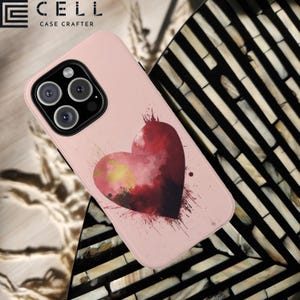 May include: A pink phone case with a watercolor-style red heart design. The case has a raised camera bump and the text "CELL CASE CRAFTERS" is printed on the top.