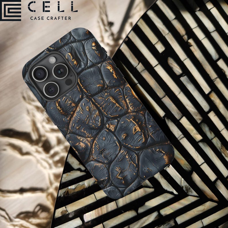 May include: A black and gold phone case with a crocodile skin pattern. The case is made by the company "CELL CASE CRAFTERS".