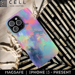 May include: A phone case with a colourful, abstract design in shades of pink, blue, and yellow. The case is designed for an iPhone 13 or newer model and features MagSafe compatibility. The case has the "CELL CASE CRAFTER" logo.