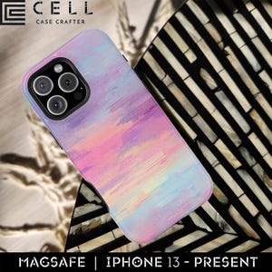 Könnte beinhalten: Smartphone-Hülle mit einem farbenfrohen, abstrakten Design in Rosa-, Lila- und Blautönen. Die Hülle hat ein schwarzes Kameramodul und den Text "MAGSAFE | IPHONE 13 - PRESENT". Der Markenname "CELL CASE CRAFTER" ist oben zu sehen.