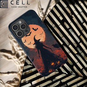 May include: A black phone case with a Halloween-themed design. The design features a witch standing in front of a full moon with bats flying around it. There are also pumpkins and crows in the design.