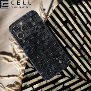 May include: A black phone case with a mosaic pattern. The case is made of a durable material and has a sleek design. The case is compatible with the iPhone 13 Pro Max. The case is shown on a table with a black and white patterned surface. The text "CELL CASE CRAFTERS" is visible in the top left corner of the image.