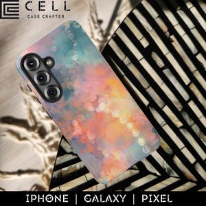 May include: A phone case with a colorful watercolor design in shades of pink, orange, and blue. The case has a camera cutout and the text "IPHONE | GALAXY | PIXEL". The case is from the brand "CELL CASE CRAFTER".