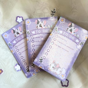 May include: Three rectangular to-do list notepads in a light purple color palette. Each notepad features a cartoon chinchilla illustration, a header reading TO DO, and a checklist with German text including Einkaufen and Chinchillas kraulen.