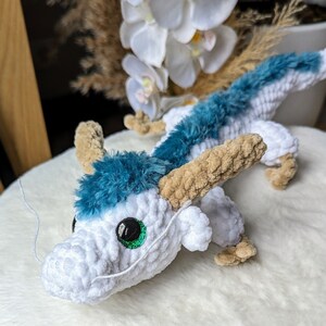 May include: A white and blue crocheted dragon toy with a green eye. The dragon has a long, curled tail and a small, pointed snout.