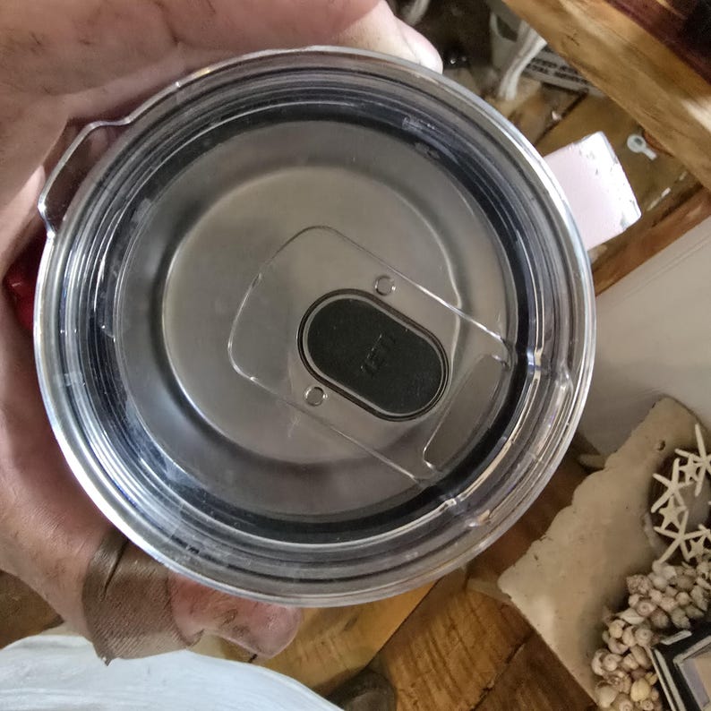 K&ouml;nnte beinhalten: Ein klarer Kunststoffdeckel mit schwarzem Schieber und Edelstahl-Innenraum. Der Deckel hat einen transparenten Kunststoffgriff und eine schwarze Gummidichtung. F&uuml;r einen Becher oder Reisebecher.