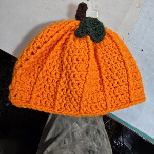 Puede incluir: Sombrero de calabaza de punto de color naranja con un tallo verde y marr&oacute;n.