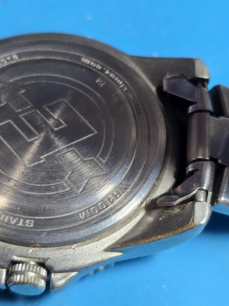 May include: The back of a silver watch with a stainless steel band. The watch face has a black background with white markings. The watch has a date window at the 3 o'clock position. The watch is water resistant and has a screw down crown. The watch has a black leather band.