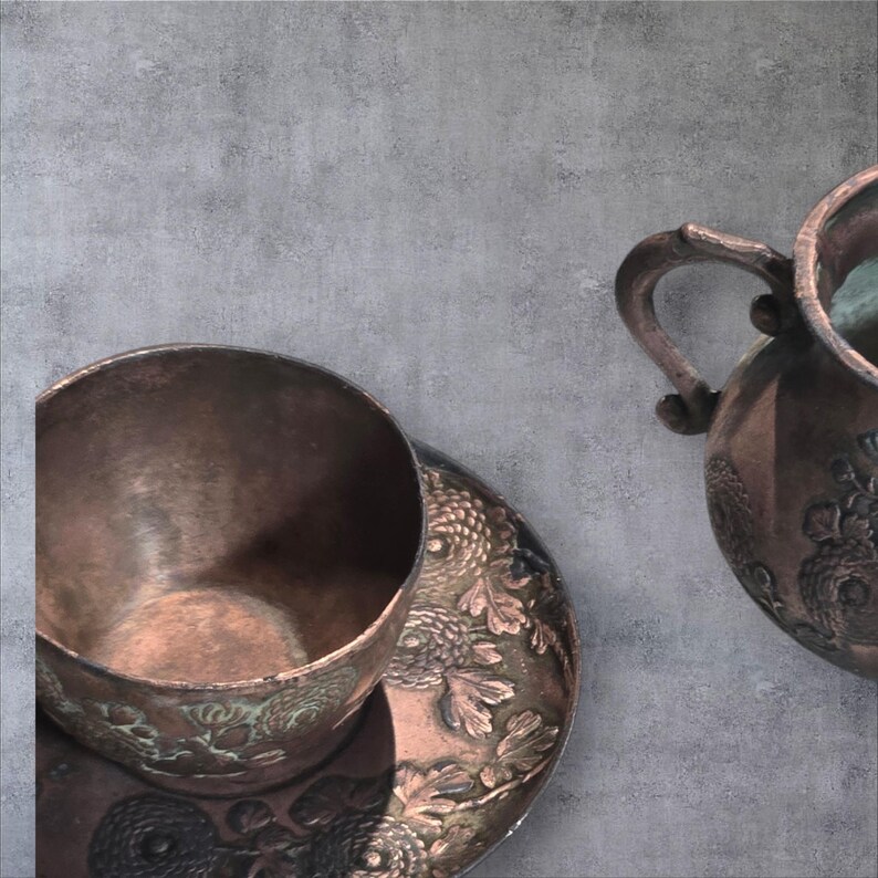 Op de afbeelding: Een koperen theekopje en schotel met een bloemenmotief, en een koperen kan met een bloemenmotief.