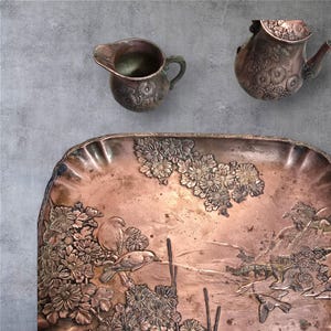 Op de afbeelding: Een koperen dienblad met een sierlijk ontwerp van bloemen en vogels. Het dienblad heeft een licht verhoogde rand en een gegolfde rand.