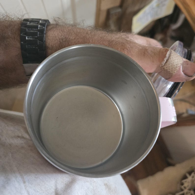 K&ouml;nnte beinhalten: Ein Reisebecher aus Edelstahl mit rosa Griff. Der Innenraum des Bechers ist silberfarben und die Au&szlig;enseite hat ein geb&uuml;rstetes Metall-Finish. Der Becher ist leer und sieht sauber aus.