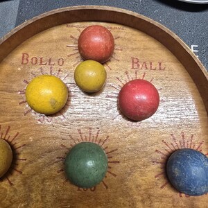 K&ouml;nnte beinhalten: Holz-Bollo-Ball-Spielbrett mit sechs bunten Kugeln. Auf dem Holzbrett steht "Bollo Ball". Die Kugeln sind rot, gelb, gr&uuml;n und blau.