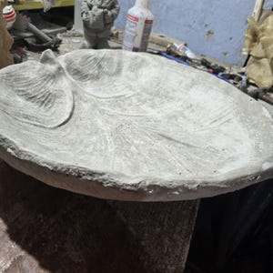 May include: A light grey concrete bowl shaped like a large leaf with a textured surface. The bowl features a prominent central vein and smaller branching veins embossed into the material, with a rough, uneven edge and a shallow, wide basin.