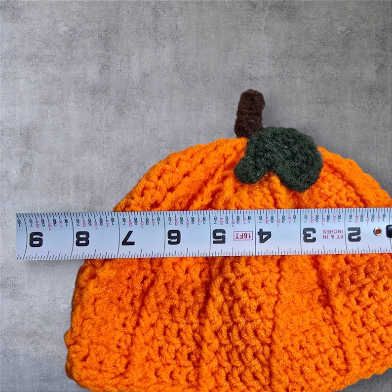 Puede incluir: Sombrero de calabaza de punto de ganchillo naranja con un tallo y una hoja de fieltro verde. El sombrero mide aproximadamente 15 cm de di&aacute;metro.