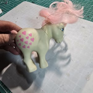May include: A light green My Little Pony toy with pink hair and a pink heart pattern on its rear end.