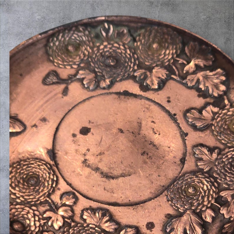 Op de afbeelding: Een koperen dienblad met een reli&euml;fdesign van chrysanten en bladeren. Het dienblad heeft een licht verweerde, verouderde uitstraling.