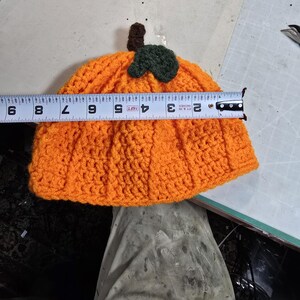 Puede incluir: Sombrero de calabaza de punto de ganchillo naranja con un tallo y una hoja de punto de ganchillo verde. El sombrero mide 23 cm de di&aacute;metro.