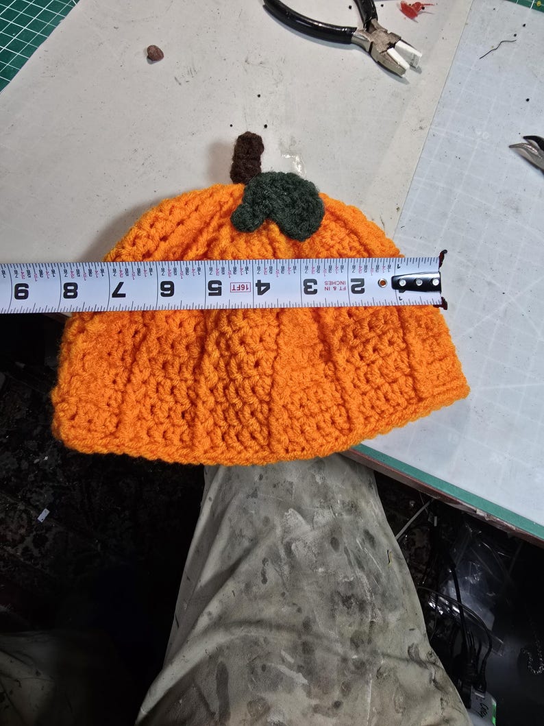 Puede incluir: Sombrero de calabaza de punto de ganchillo naranja con un tallo y una hoja de punto de ganchillo verde. El sombrero mide 23 cm de di&aacute;metro.