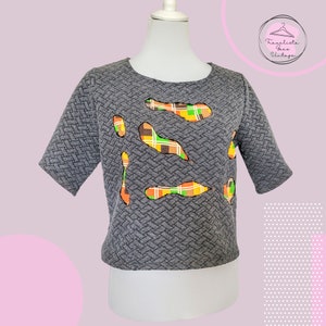 Può includere: Top grigio a maniche corte con una trama tessuta e un design patchwork di tessuto a quadri arancione, verde e marrone.