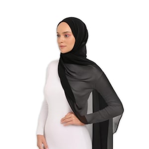 May include: A black sheer scarf draped over a person's shoulders and head. The scarf is made of a lightweight fabric and has a flowing, elegant look.
