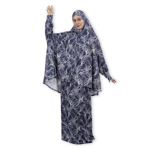 May include: A navy blue prayer dress with a white tree branch pattern. The dress has long sleeves and a long skirt. The dress is worn with a matching navy blue hijab.