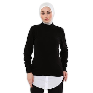 Peut inclure: Un pull noir à col roulé et manches longues, avec une chemise blanche visible en dessous. La personne porte un voile blanc. Le pull est de couleur unie et semble être fait d'une matière douce.