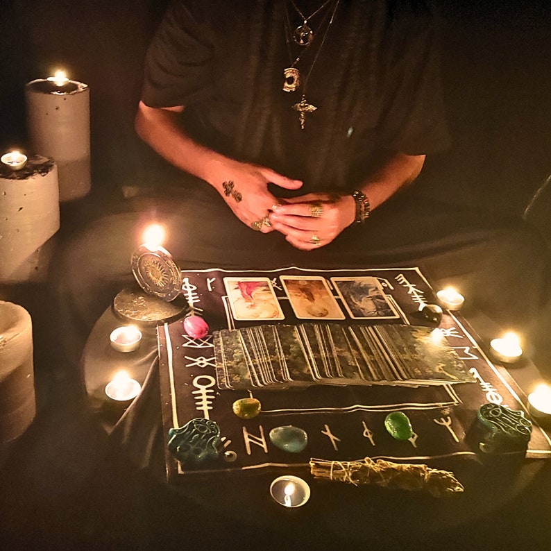 May include: A tarot card reading spread laid out on a black cloth with runes and crystals. The spread is lit by candlelight and includes a variety of cards, including the Tower, the World, and the Star.