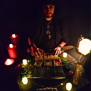 May include: A tarot card reading in a dimly lit room with candles and incense. The cards are spread out on a table, and the person is holding their hands over them.
