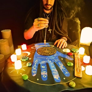 May include: A blue and gold hand-shaped divination board with a compass in the center. The board is surrounded by candles, incense, and other tools for divination.