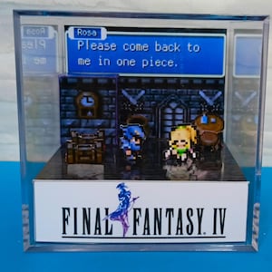 Può includere: Un diorama 3D di una scena di Final Fantasy IV, con i personaggi Rosa, Cecil e Rydia. Il diorama è racchiuso in una scatola di acrilico trasparente con una base nera. Il testo "FINAL FANTASY IV" è stampato sulla base. Il diorama include un fumetto con il testo "Rosa: Per favore, torna a casa sano e salvo."