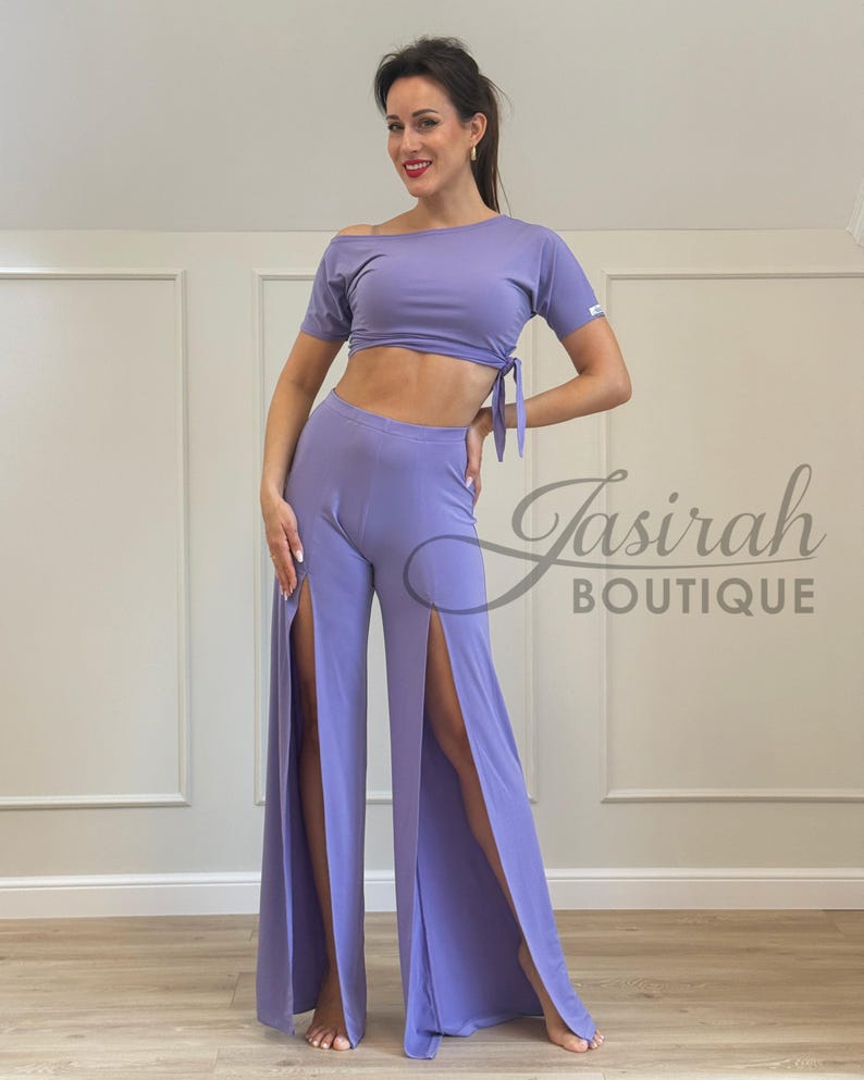 May include: A lavender two-piece outfit featuring a crop top with an off-the-shoulder design and tie detail, paired with wide-leg pants with high slits. The outfit is made of a soft, flowing fabric. The text "Jasirah Boutique" is visible.