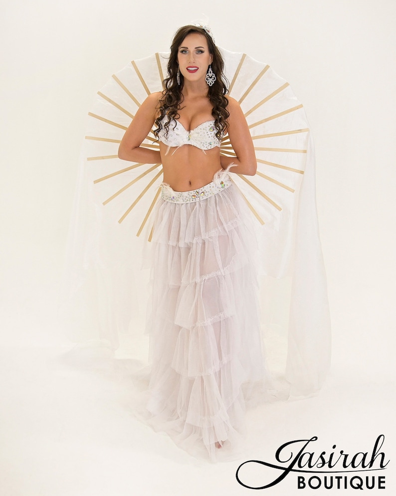 Puede incluir: Un traje de danza del vientre blanco con una falda escalonada y sujetador y cintur&oacute;n adornados. El disfraz incluye un gran accesorio en forma de abanico con detalles dorados. Tambi&eacute;n se incluye el texto "Jasirah Boutique".