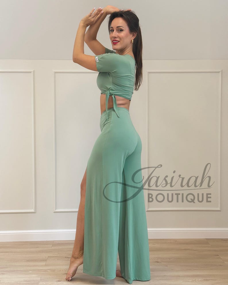 May include: A mint green two-piece outfit, featuring a short-sleeved crop top with a tie detail and high-waisted, wide-leg pants with a side slit. The outfit is made of a soft, flowing fabric. The text "Tasirah Boutique" is visible.