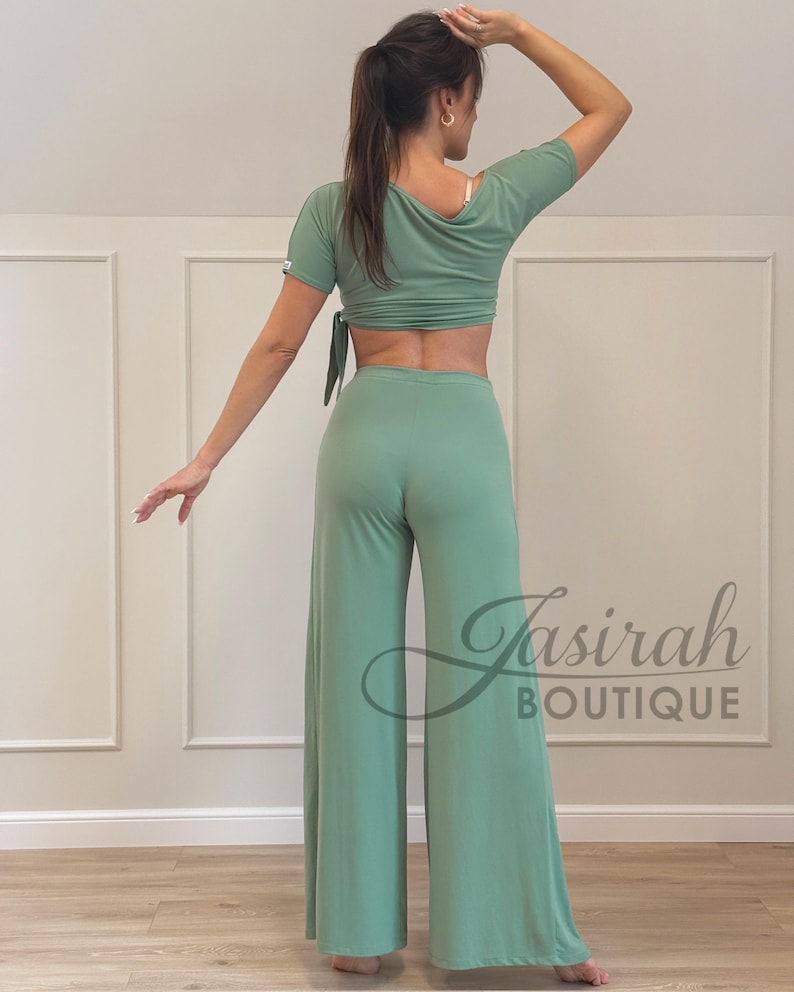 May include: A sage green two-piece outfit featuring a crop top with short sleeves and a tie closure, paired with wide-leg pants. The outfit is made of a soft, flowing fabric. The logo "Jasirah Boutique" is visible.