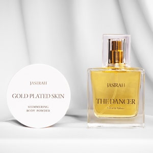 May include: A cosmetic product set featuring a round, white container labeled "JASIRAH GOLD PLATED SKIN SHIMMERING BODY POWDER" and a square perfume bottle with "JASIRAH THE DANCER Extrait de Parfum" text.